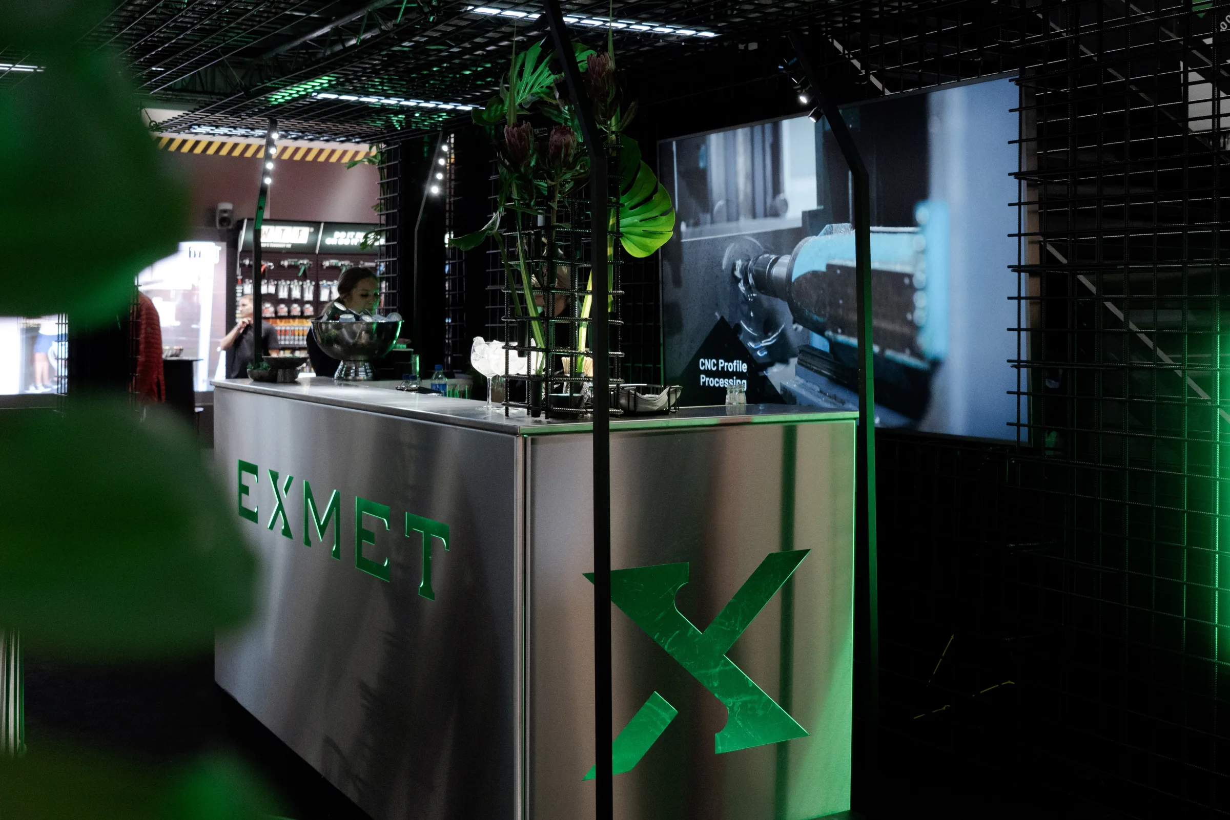 Exmet Group stand glowing green at FinnBuild, with a counter and CNC profile processing screen